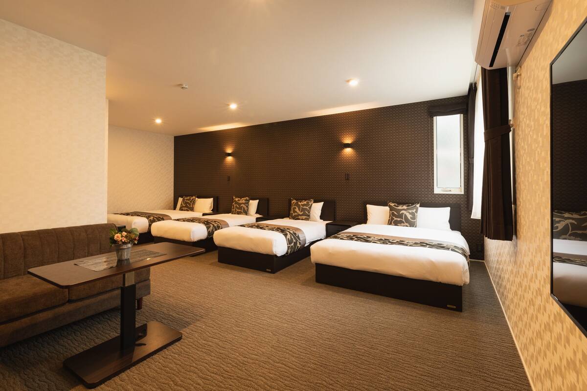 Une chambre d’hôtel avec trois lits, un canapé, une petite table et une grande fenêtre.