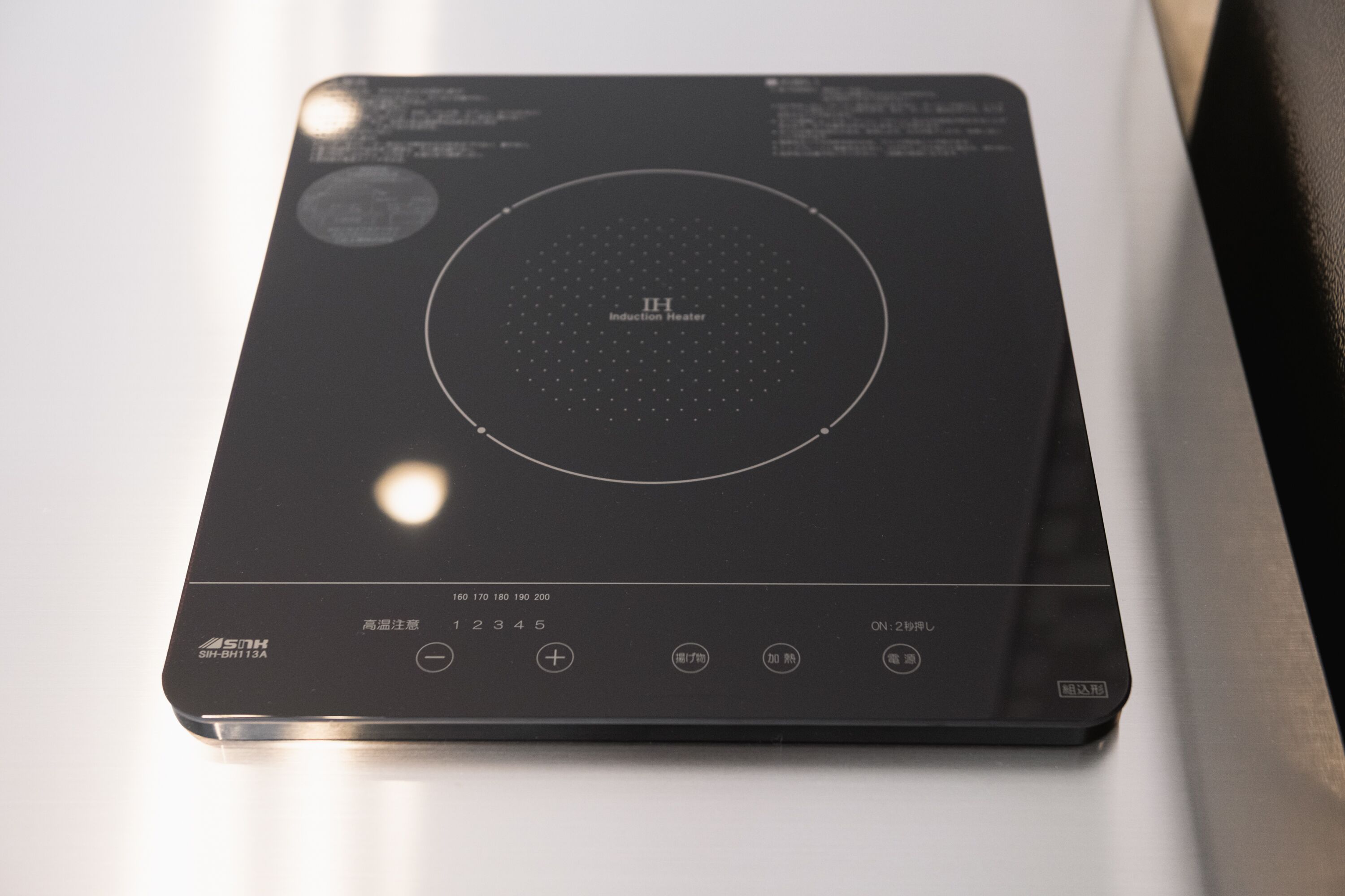 A black induction heater with a circular control panel and multiple buttons.