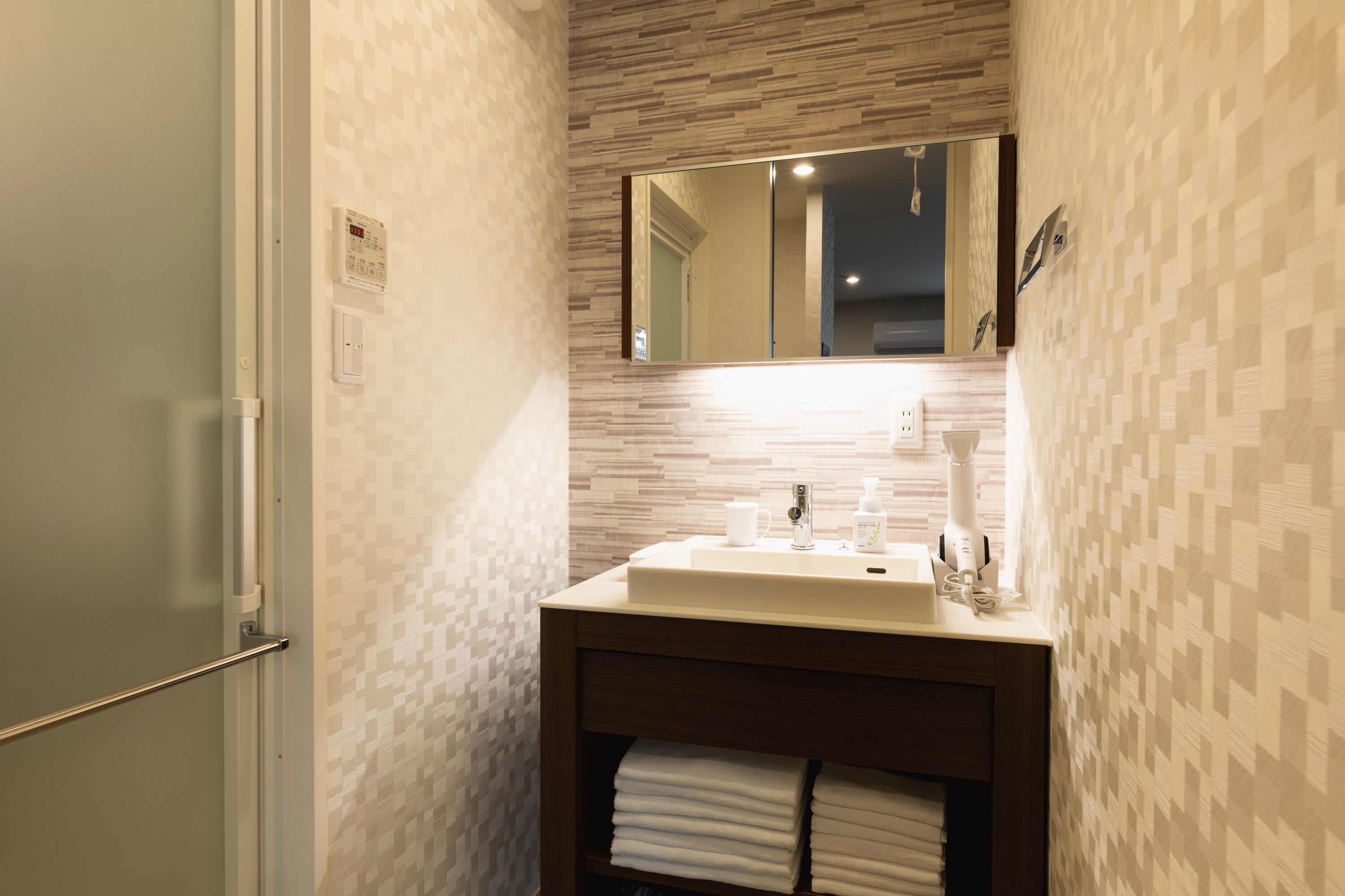 Un baño con pared de azulejos, un lavamanos con espejo y un toallero con toallas dobladas.