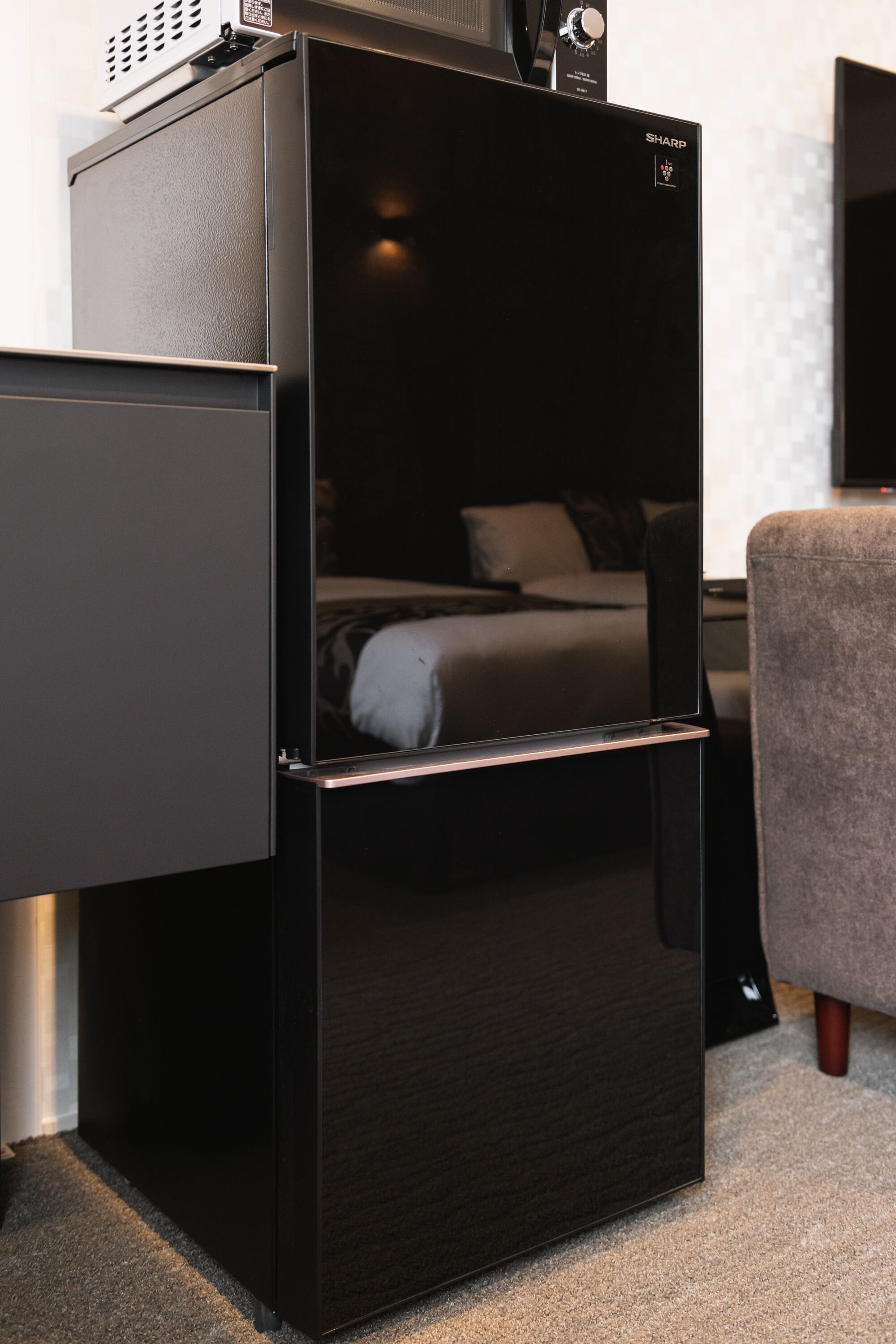 Een compacte, moderne kamer met een ingebouwde koelkast en magnetron, een klein zithoekje en een bed met hoofdeinde.