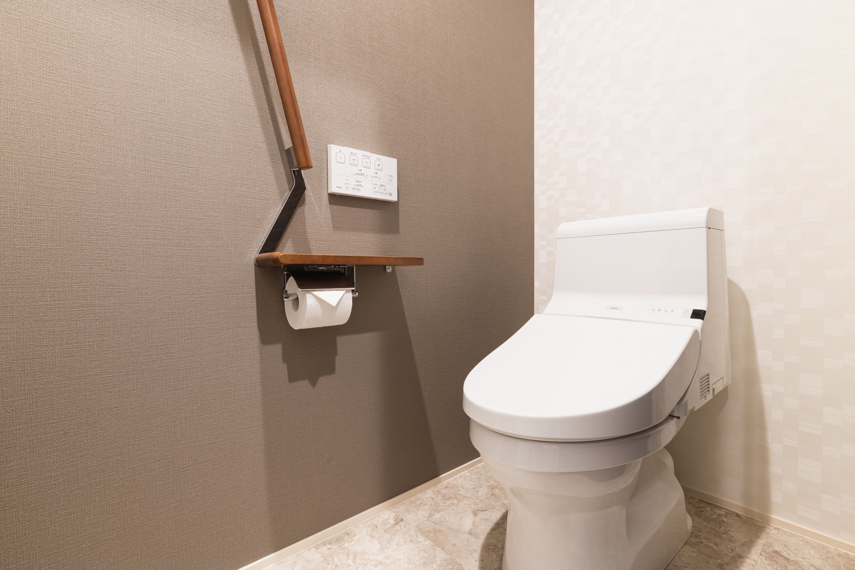 A modern bathroom with a toilet, a towel dispenser, and a wall-mounted electrical outlet.