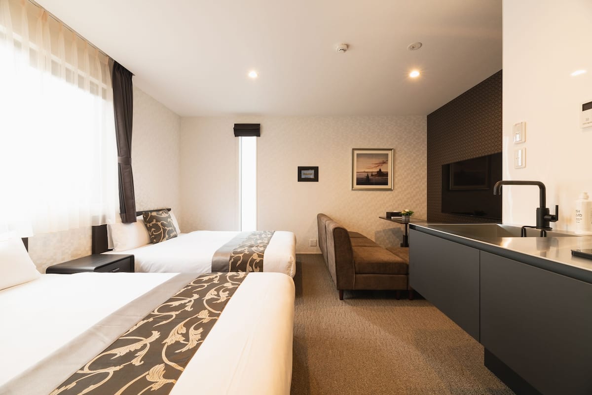 Une chambre d’hôtel avec deux lits, un canapé, une t élévision et une kitchenette.