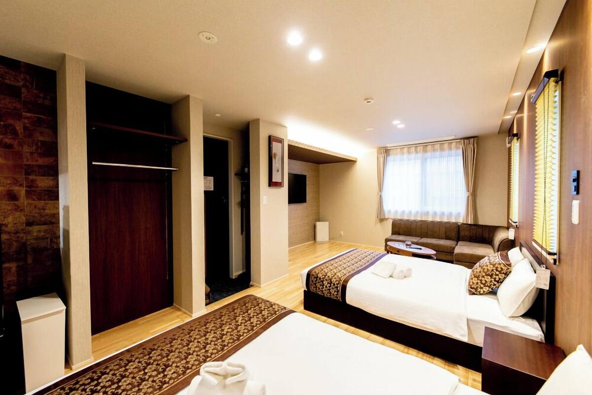A hotel room with two beds, a sofa, a small table, and a wardrobe.