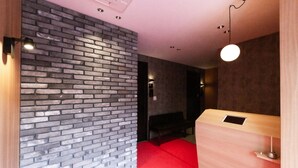A modern hotel room with a brick wall, a red carpet, a wooden reception desk, and a bench. - Grand Base Hiroshima Hikarimachi (Hiroshima)