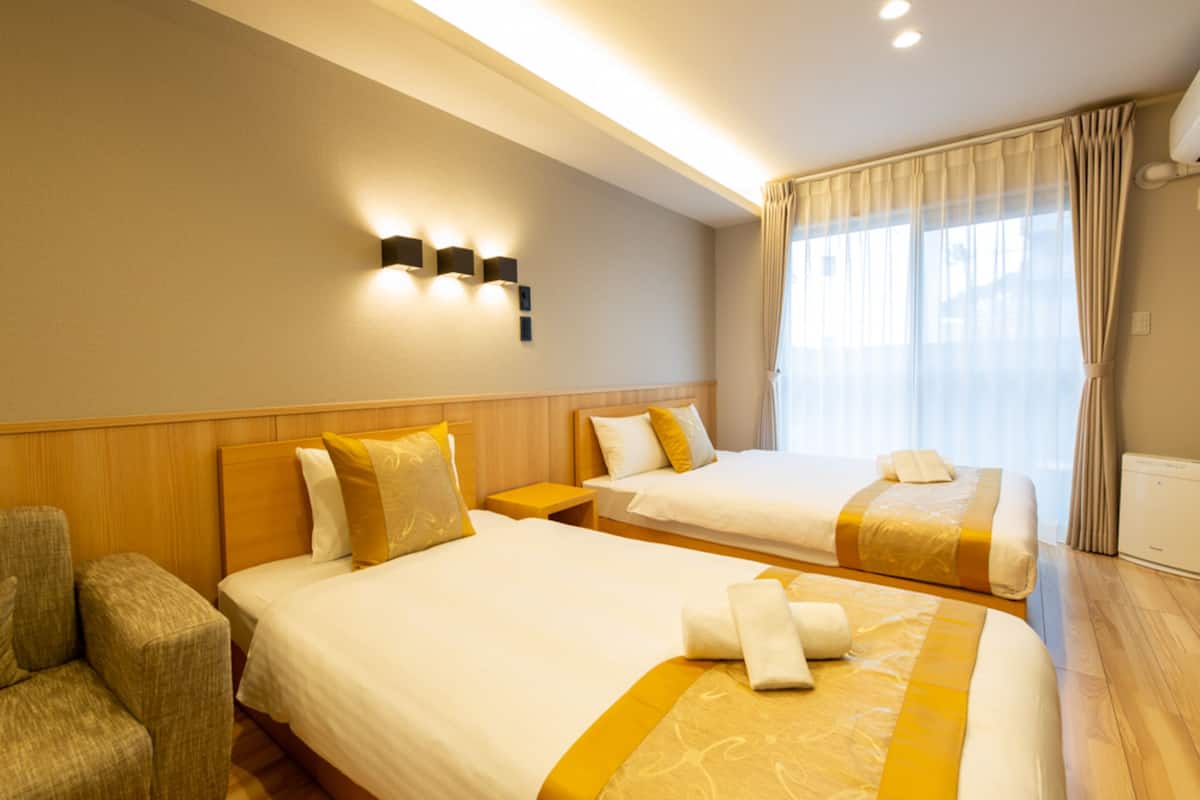 A hotel room with two beds, a sofa, a nightstand, and a window with curtains.