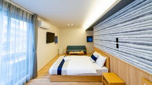 A hotel room with a large bed, a wooden bench, a green sofa, and a wall-mounted TV. - Grand Base Hiroshima Hikarimachi (Hiroshima)