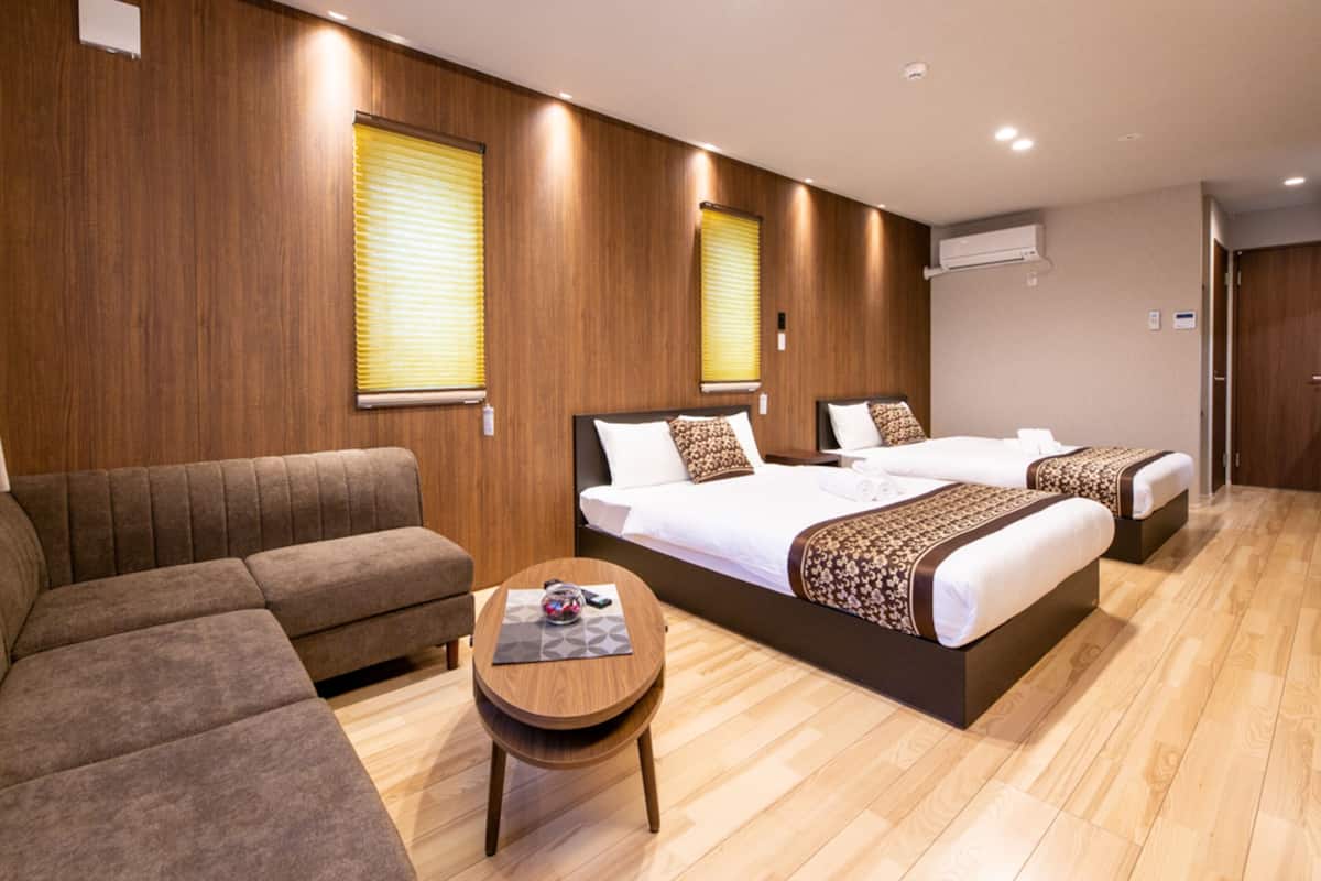 A hotel room with two beds, a sofa, a round wooden table, and wooden walls.