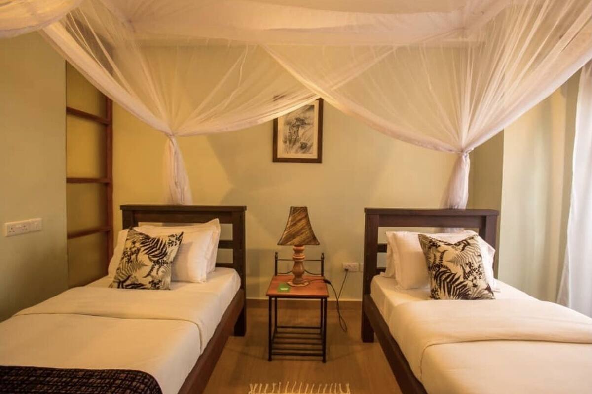 A room with two beds, a nightstand, a lamp, and a mosquito net.