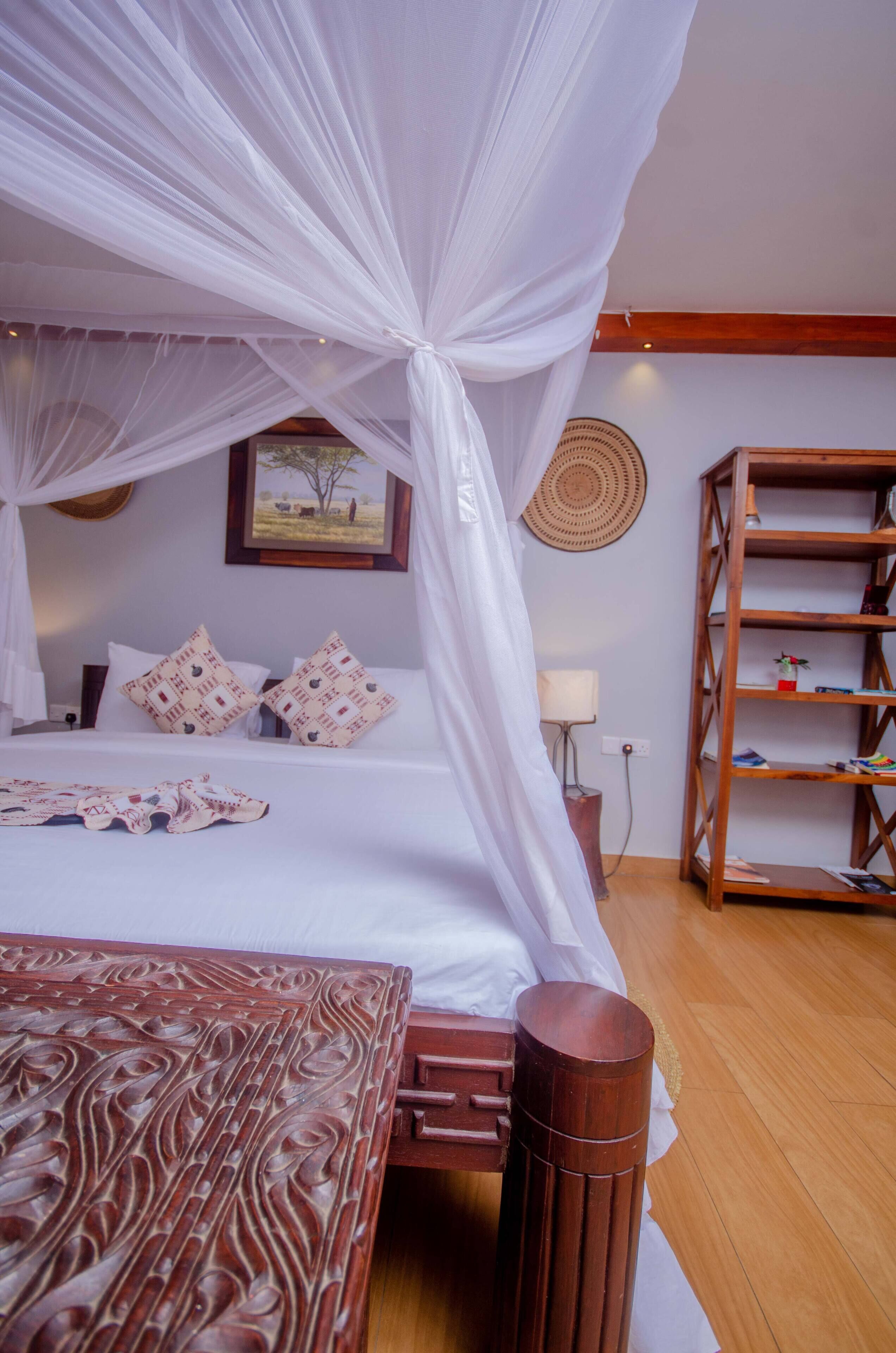 A bedroom with a canopy bed, a wooden headboard, a bedside table, a lamp, a wall-mounted shelf, and a framed picture on the wall.