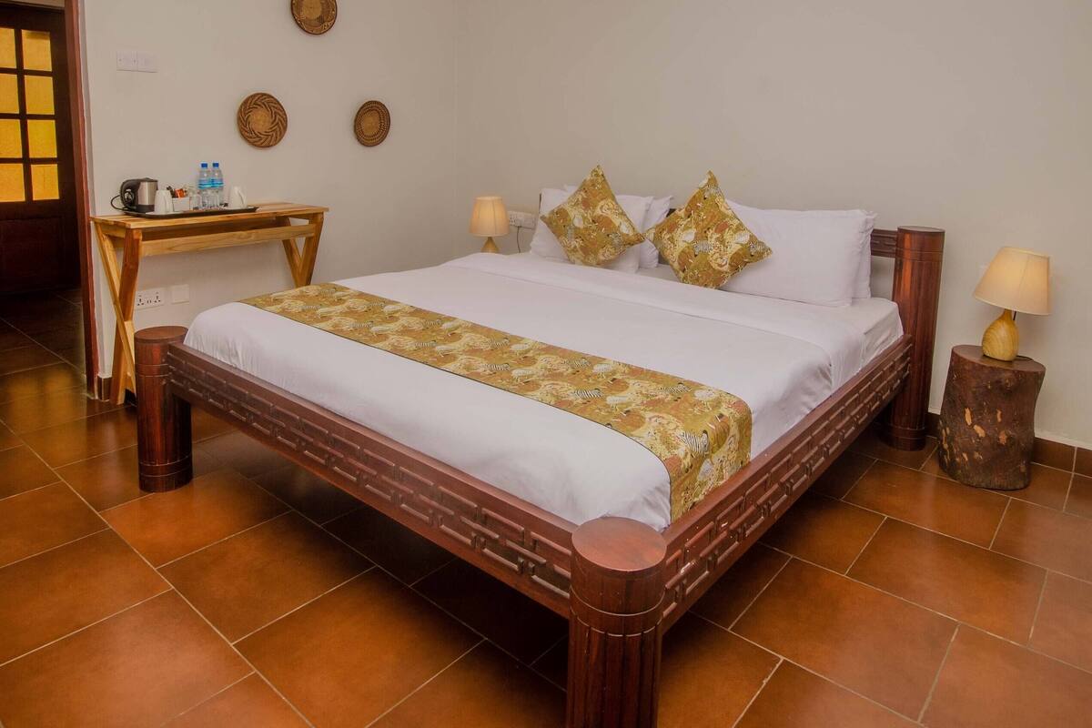 A hotel room with a large bed, a wooden desk, a small table, and a lamp.