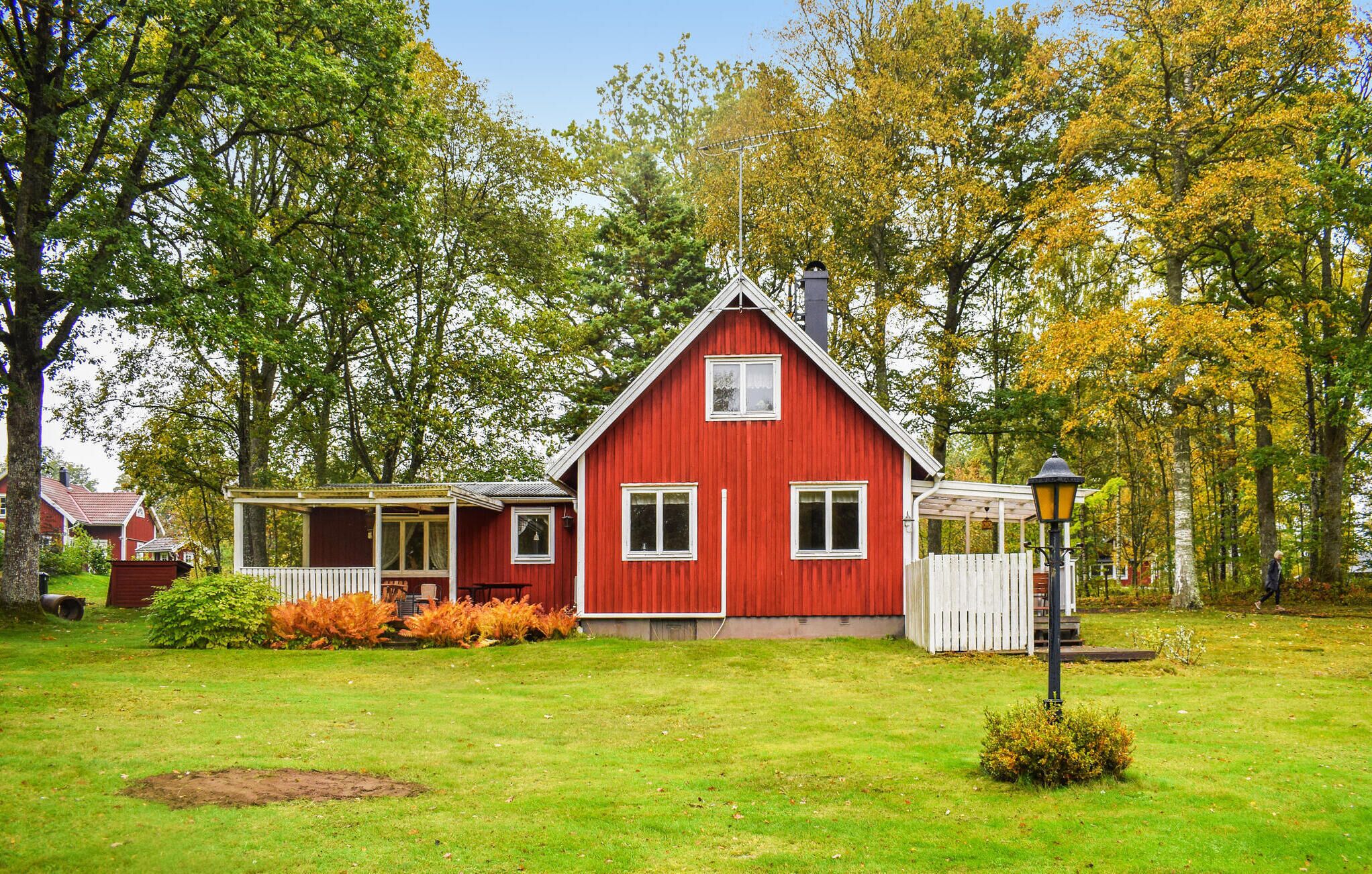 A red house with a white porch, surrounded by trees and a grassy yard.