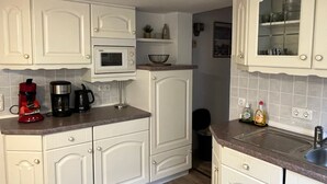 Una cocina con armarios blancos, microondas, cafetera y lavamanos.