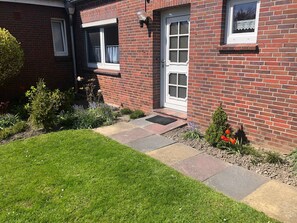 A brick house with a well-maintained garden, a front door, and a window with a lace curtain.