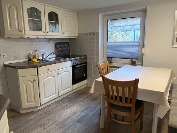 A kitchen with white cabinets, a black oven, a sink, and a dining table with chairs.