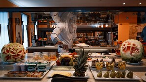 A buffet with various food items and a chef preparing food in the background.