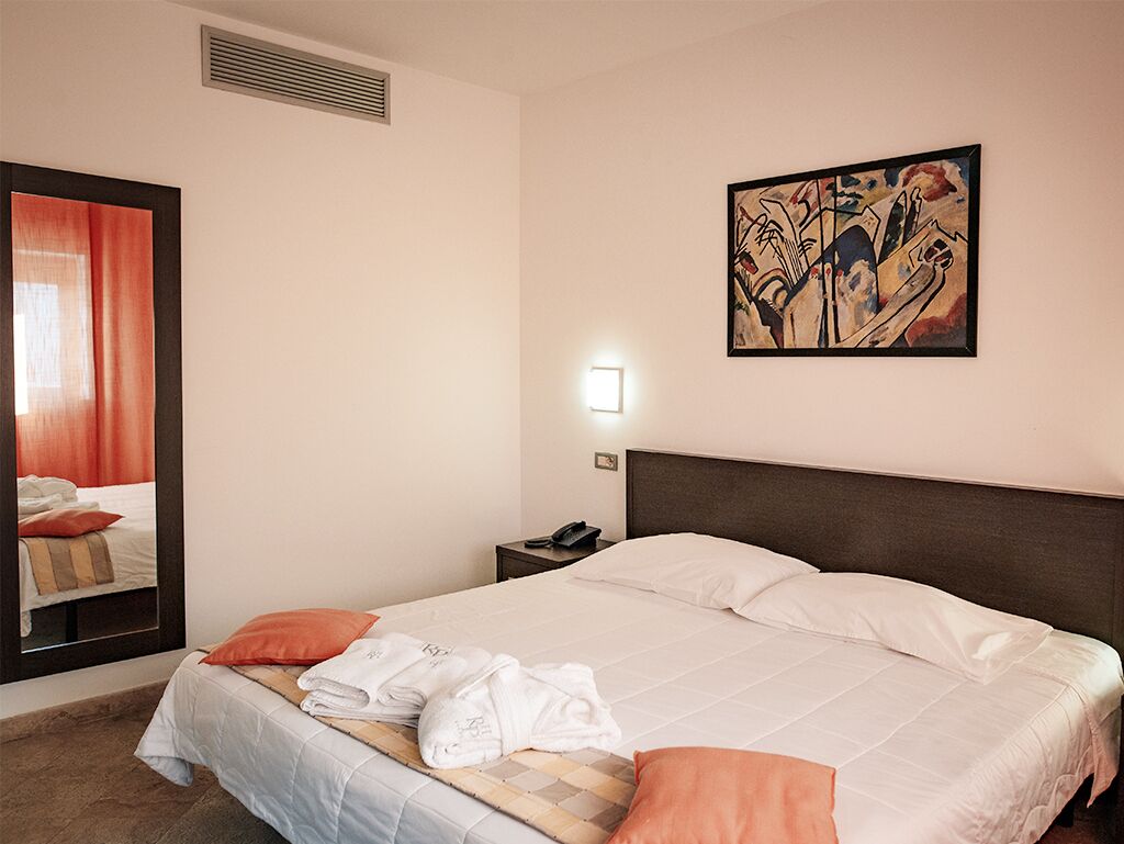 Een hotelkamer met een bed, een nachtkastje, een spiegel en een schilderij aan de muur.