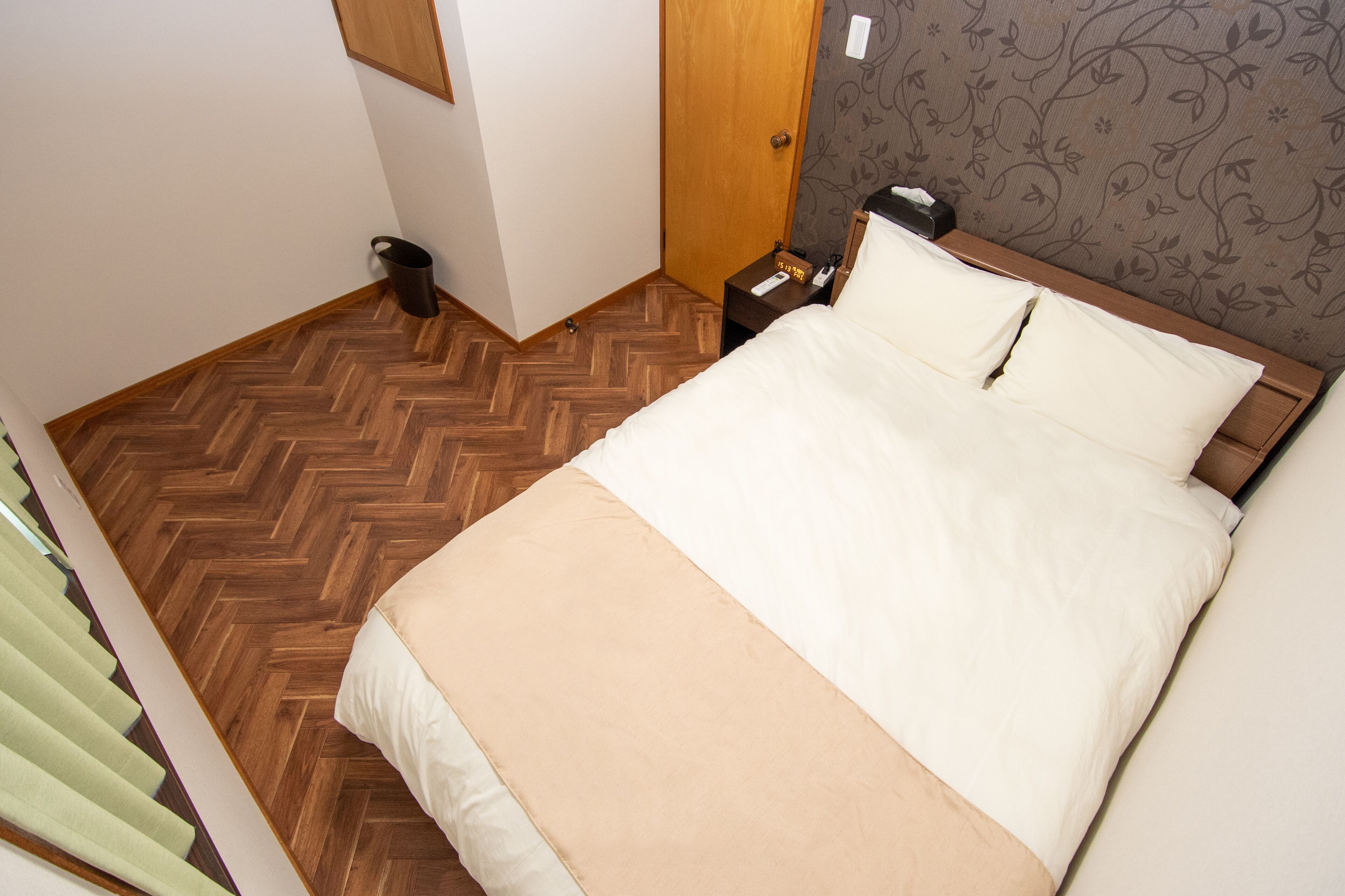 Un lit bien fait, avec une tête de lit en bois, une table de chevet sur laquelle se trouvent un téléphone et une lampe, et un papier peint à motifs sur le mur.