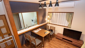 Un espacio habitable pequeño con una mesa de comedor de madera, cuatro sillas, un televisor y un espejo grande.