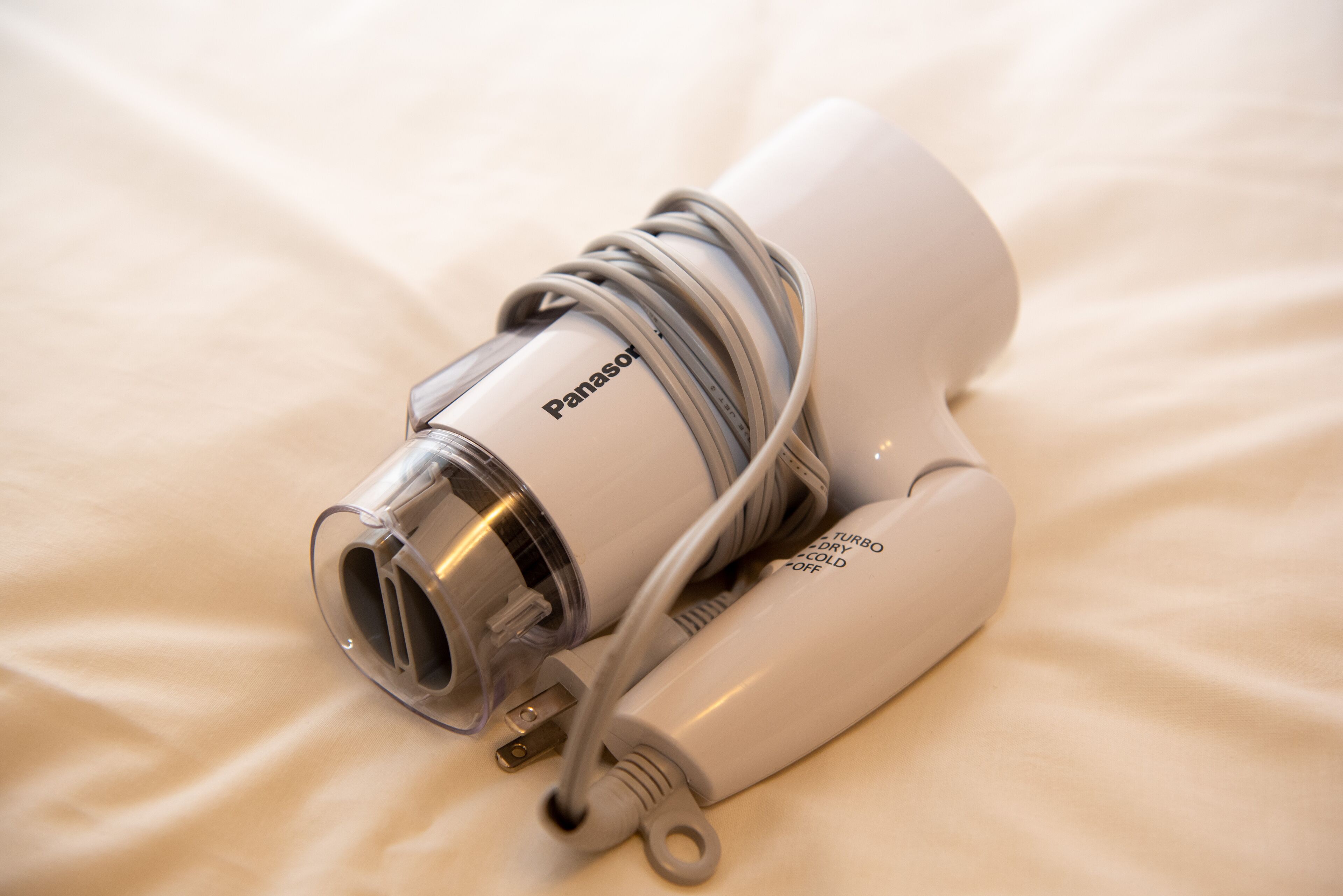 A white Panasonic hairdryer with a cord and a power adapter on a bed.