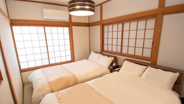 Una habitación tradicional japonesa con dos camas, vigas de madera, puertas correderas shoji y un ventilador de techo.