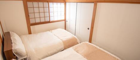 A room with two beds, a window with wooden frames, and a ceiling-mounted air conditioner.