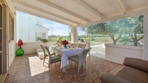 Eine überdachte Terrasse mit Tisch für zwei Personen, Korbstühle und Blick auf die Landschaft.
