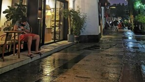 Une rue étroite avec un bâtiment dont la façade est en verre et où une personne est assise à l’extérieur.