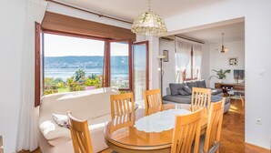 A dining area with a round wooden table, chairs, and a view of the sea through large windows. - 2 bedroom nice apartment in Trogir (Trogir)
