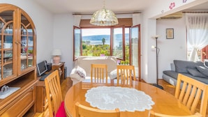 A dining area with a round wooden table, chairs, a cabinet with glass doors, a lamp, and a view of the outdoors. - 2 bedroom nice apartment in Trogir (Trogir)