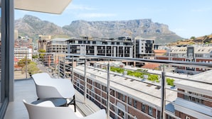 A balcony with white chairs and a view of a cityscape and mountains. - Docklands 502 (Cape Town)