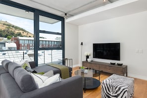 Ein modernes Wohnzimmer mit großem Fenster, einem Flachbildfernseher, einer Couch, einem Couchtisch und einem Hocker mit ZEBRA-Muster.