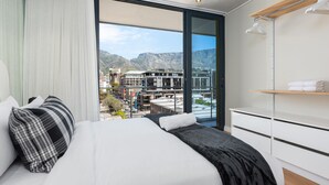 A modern hotel room with a large bed, a view of the cityscape, and a balcony with a mountain backdrop. - Docklands 502 (Cape Town)