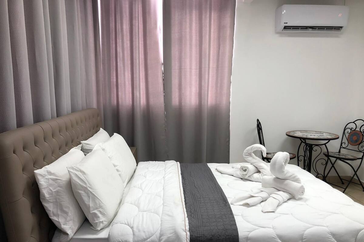 Quarto de hotel com cama, cabeceira, mesa e cadeiras, e unidade de ar condicionado.
