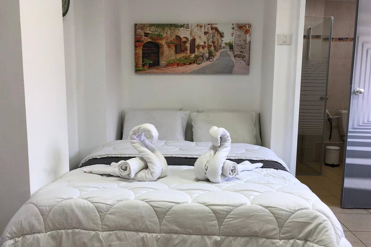 Quarto de hotel com uma cama, um quadro de uma cena urbana e uma área de chuveiro.
