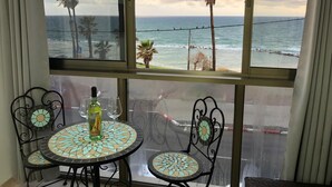 Een balkon met uitzicht op de oceaan, palmbomen en een betegelde tafel met stoelen.