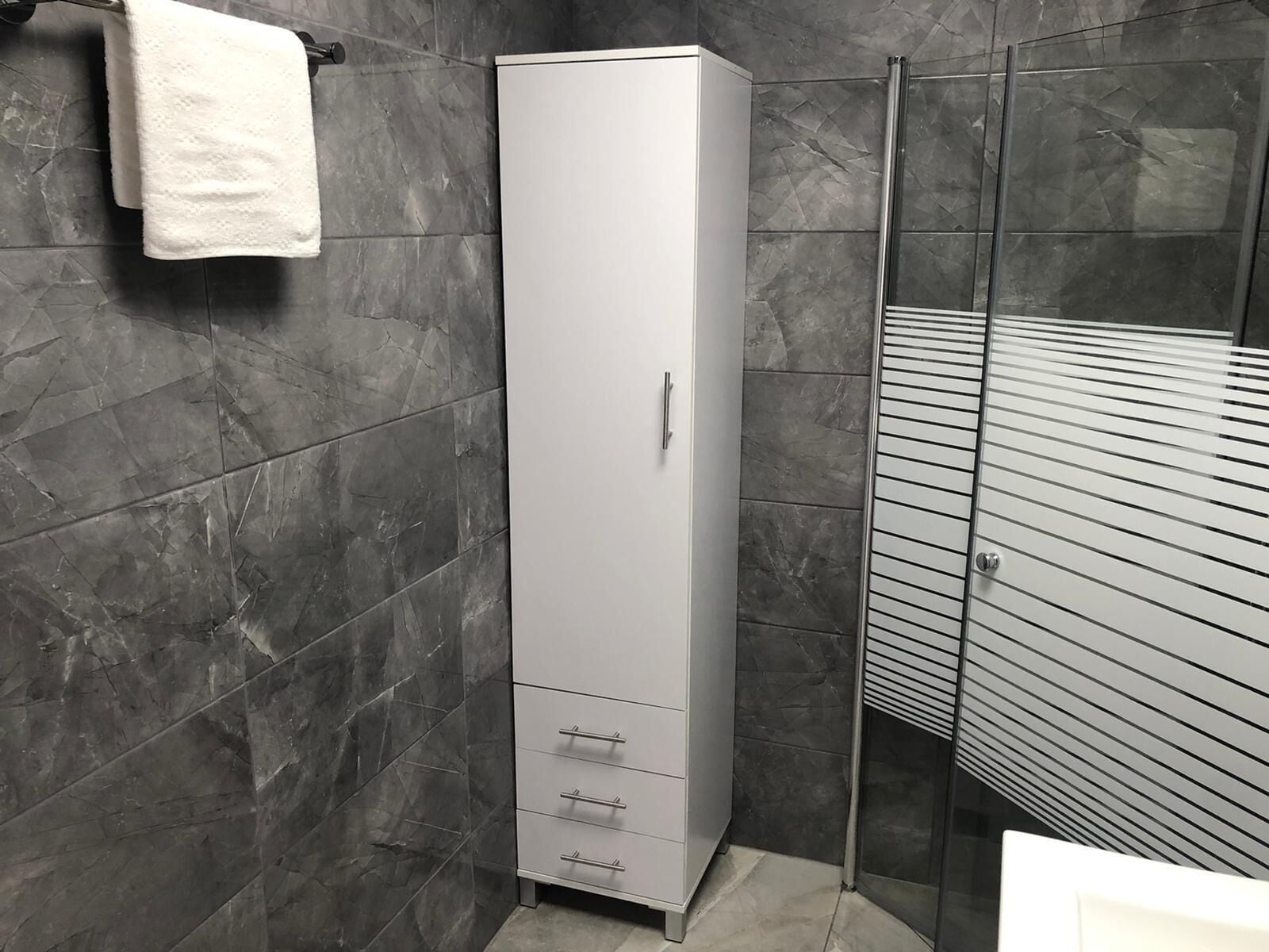 A bathroom with a tall cabinet, a glass shower enclosure, and a towel hanging on the wall.