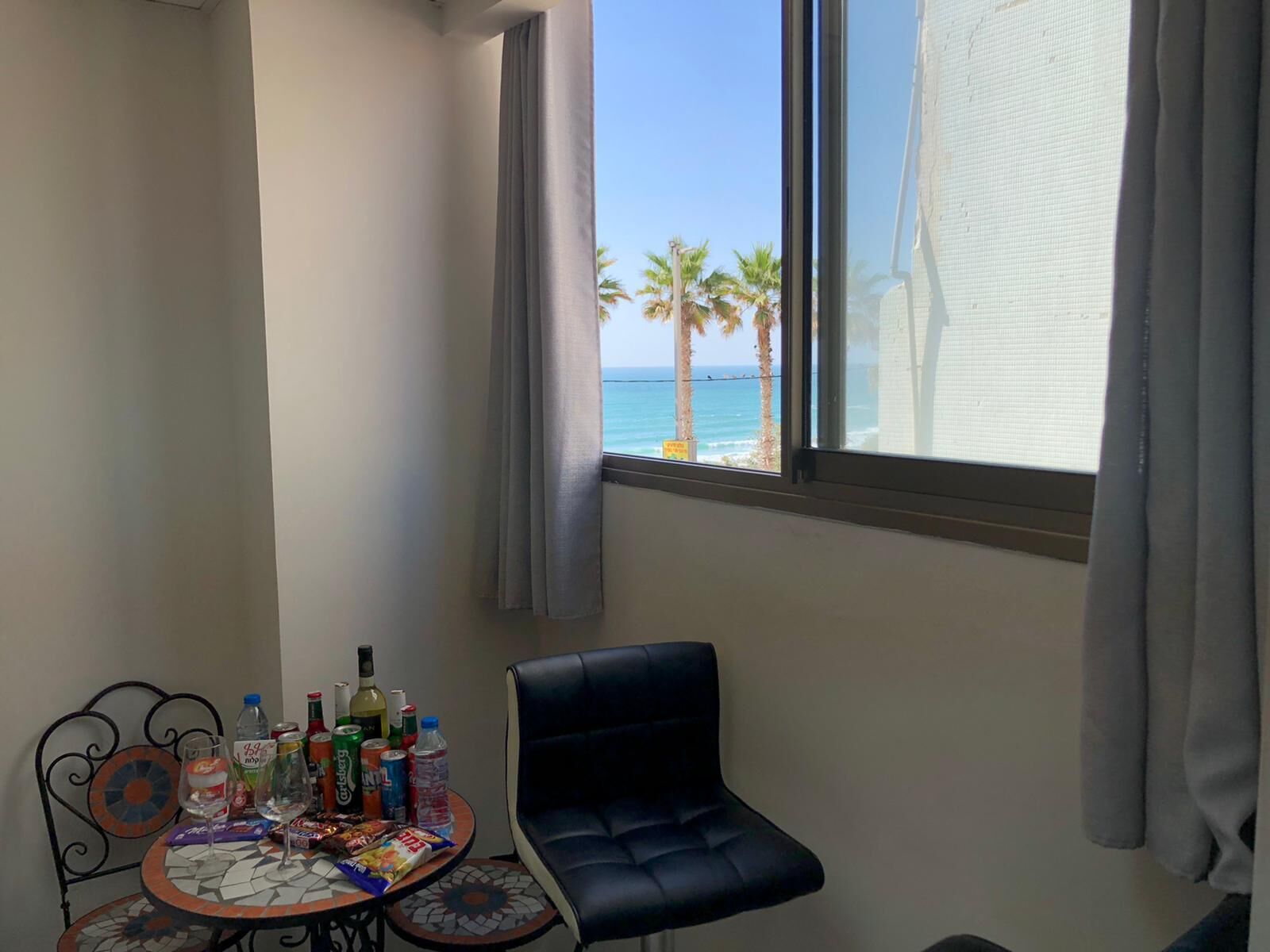 A room with a view of the ocean, a table with drinks and snacks, a black chair, and a patterned floor.