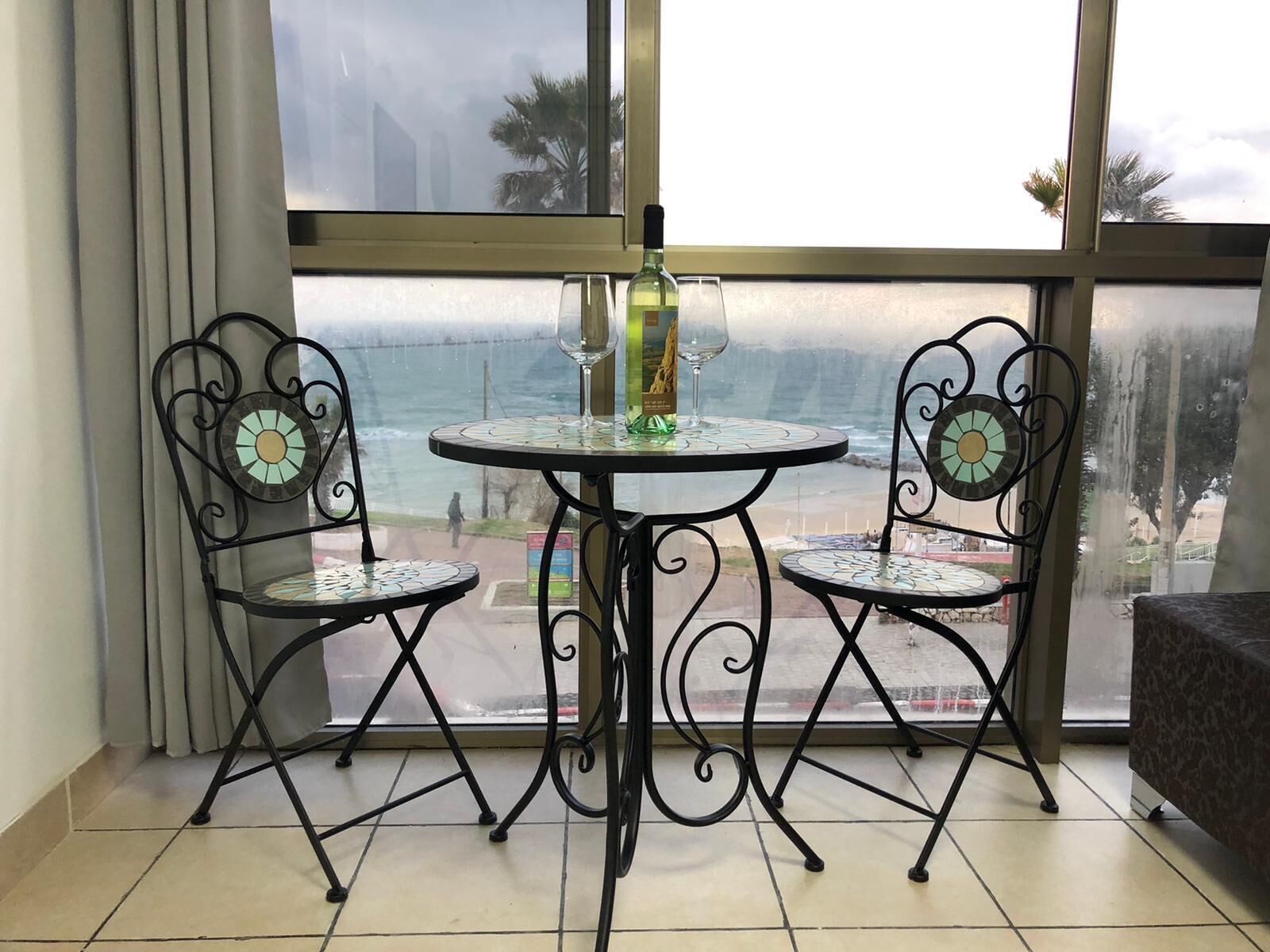 A balcony with a table and two chairs, overlooking a beach.