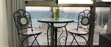 A balcony with a table and two chairs, overlooking a beach.
