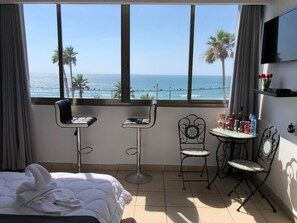 Habitació d'hotel amb un llit, una taula petita amb cadires, vista a l'oceà i un televisor a la paret.