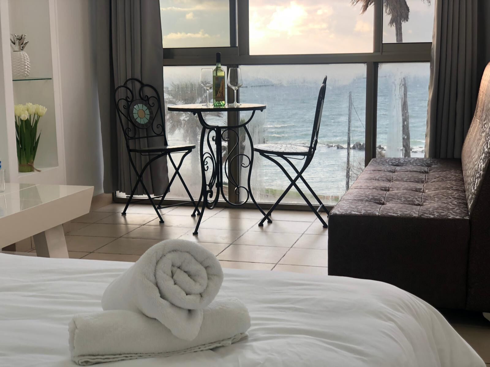 Habitación de hotel con cama, una mesita pequeña con dos sillas, vista al mar y un balcón con sofá.