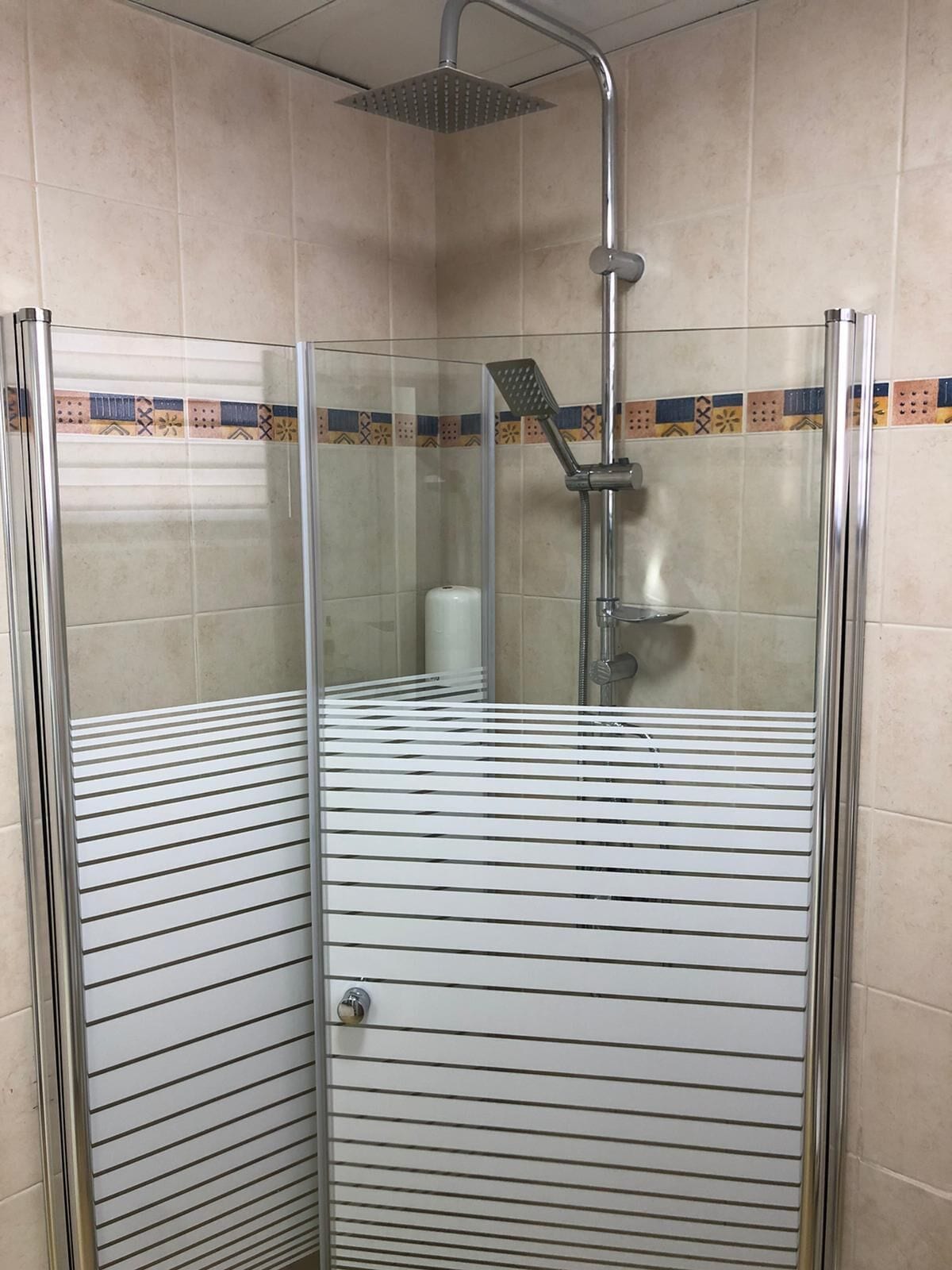 Cabina de ducha con paredes de vidrio, cabezal de ducha y ducha de mano.