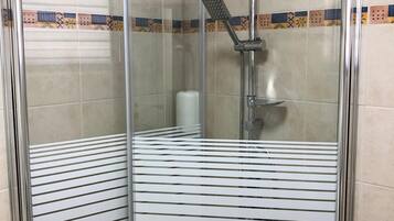 Cabina de ducha con paredes de vidrio, cabezal de ducha y ducha de mano.