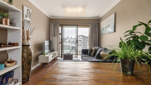 Una sala de estar moderna con piso de madera, un sofá, un televisor y un ventanal con cortinas.