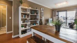 Una sala de estar moderna con una mesa de comedor de madera, una estantería blanca y un ventanal con vista a la ciudad.