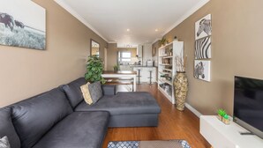 Una sala de estar moderna con un sofá modular, un televisor de pantalla plana y una cocina al fondo.