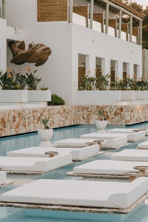 Un área junto a la piscina con sillones de descanso y una gran escultura de pez en la pared.