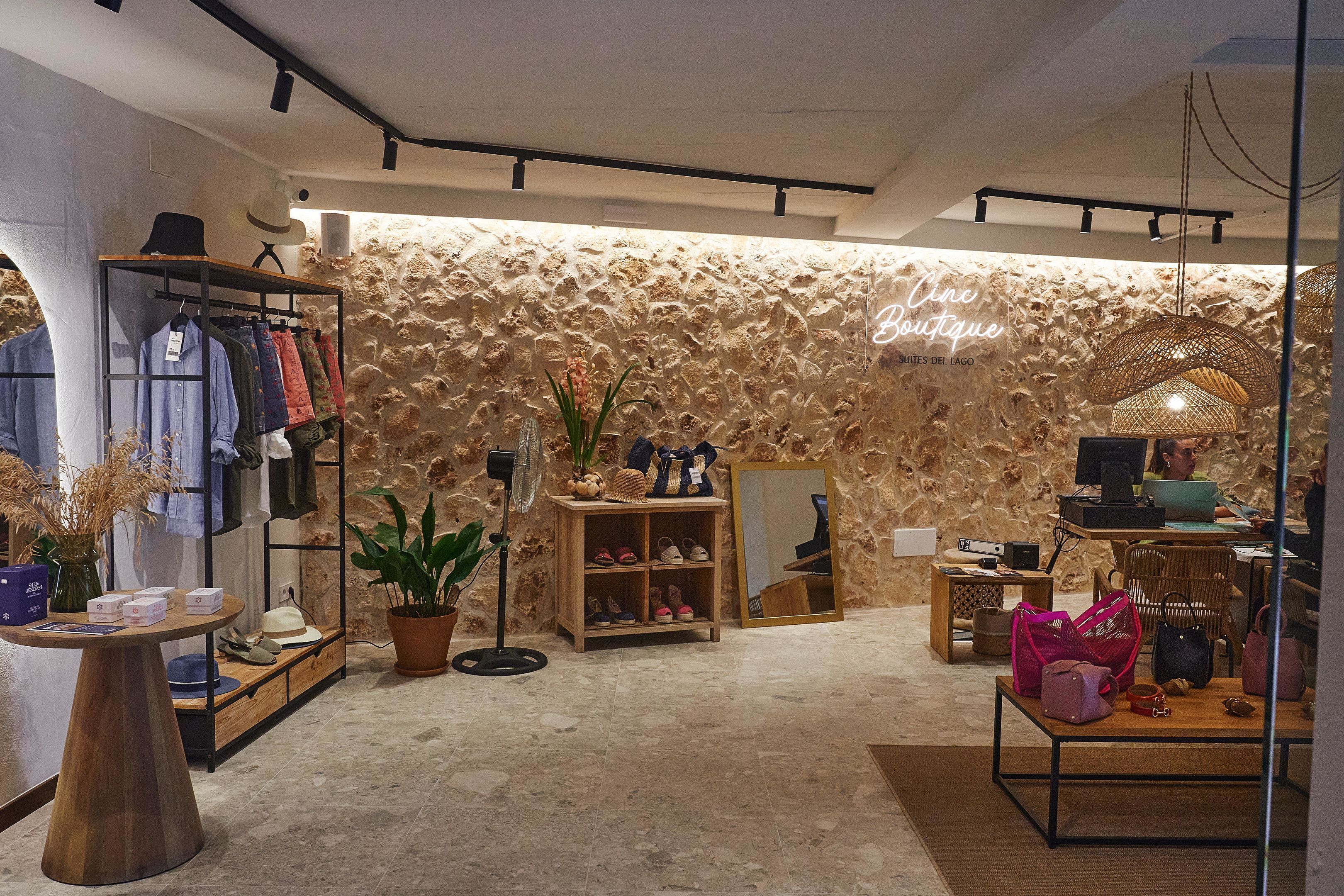 A boutique with a stone wall, clothing racks, a mirror, and a table with handbags.