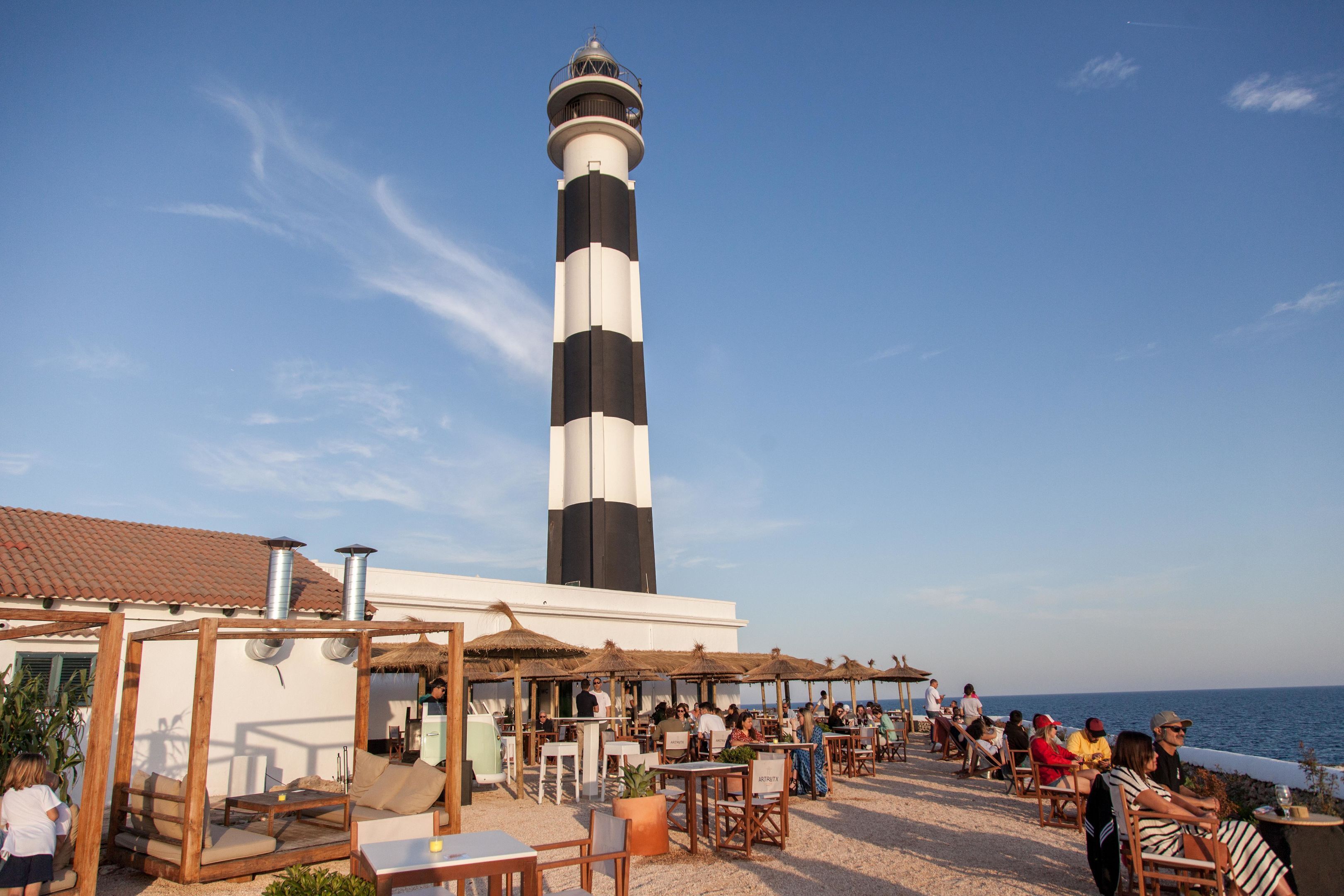 Un restaurant situé en bord de mer, avec une terrasse, un phare en arrière-plan et une vue sur l’océan.