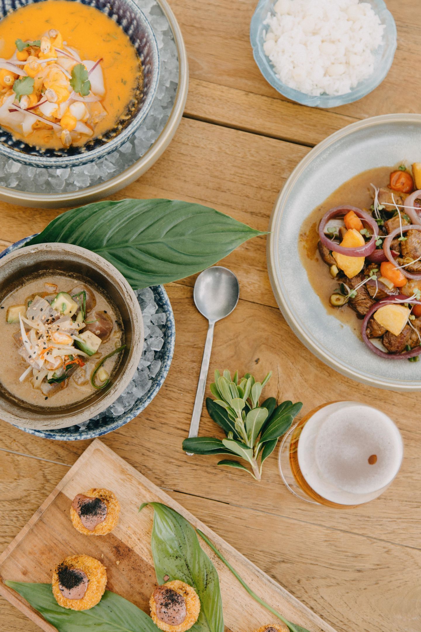 A wooden table with various dishes, including a bowl of soup, a plate of meat with vegetables, and a bowl of rice.